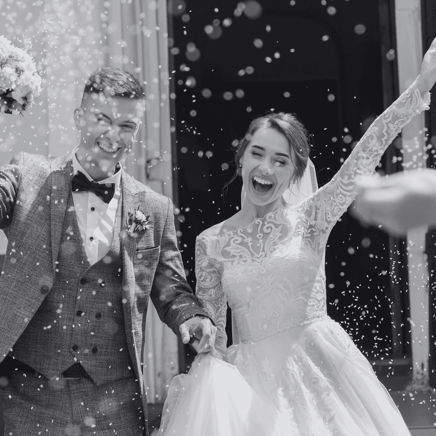 Newlywed couple celebrates joyfully under a shower of confetti outside a building.