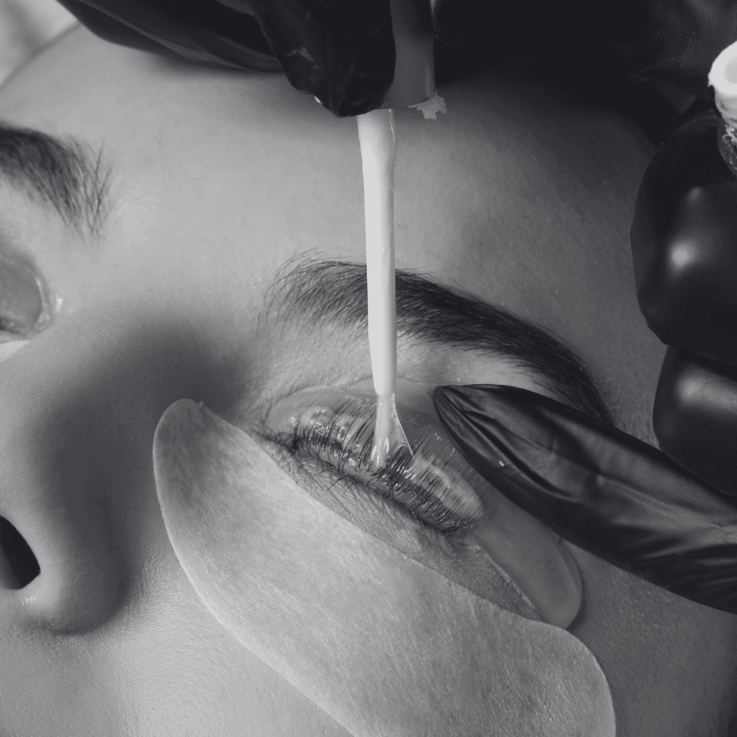 Applying lash perm solution to closed eyelid with gloved hands.