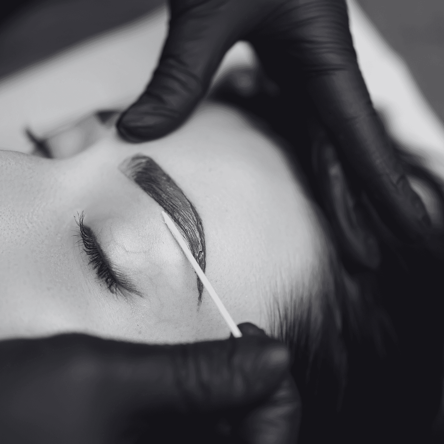 Eyebrow being shaped with precision using a cotton swab, black gloves worn by beautician.