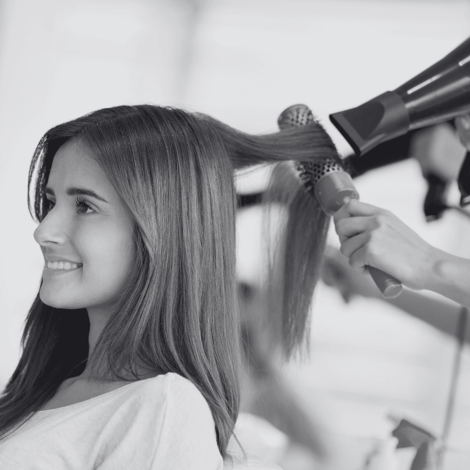 Woman getting her hair styled with a blow dryer and round brush at a salon.